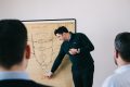 Ein Coach erklaert etwas anhand eines Whiteboards, vor ihm Sitzen Teilnehmer