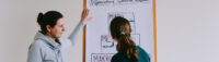 Zwei Frauen stehen vor einem Flipchart und diskutieren darüber