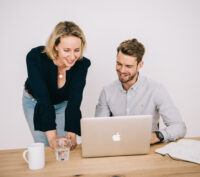 Ein Mann und eine Frau blicken in einen Laptop auf einem Schreibtisch