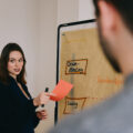 Ein Coach steht mit Karteikarten vor einem Whiteboard, im Vordergrund ein Teilnehmer