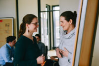 Zwei Frauen stehen vor einem Flipchart und unterhalten sich