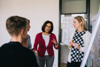 Eine Beraterin erklaert den Teilnehmern gestikuliernd die Inhalte des Coachings
