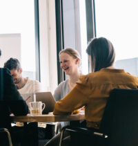 Eine lachende Frau in einer Gruppe von Menschen, die in einem Büro an einem Tisch sitzen
